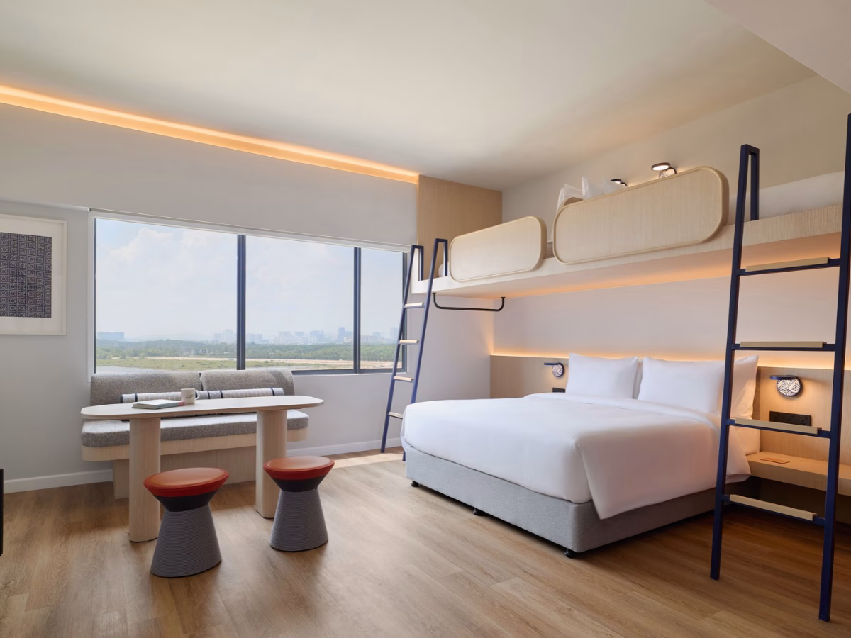 Biggy Bunk King Room at ASAI Gamuda Cove featuring a king-sized bed, an overhead bunk bed, a sofa and large windows overlooking greenery.