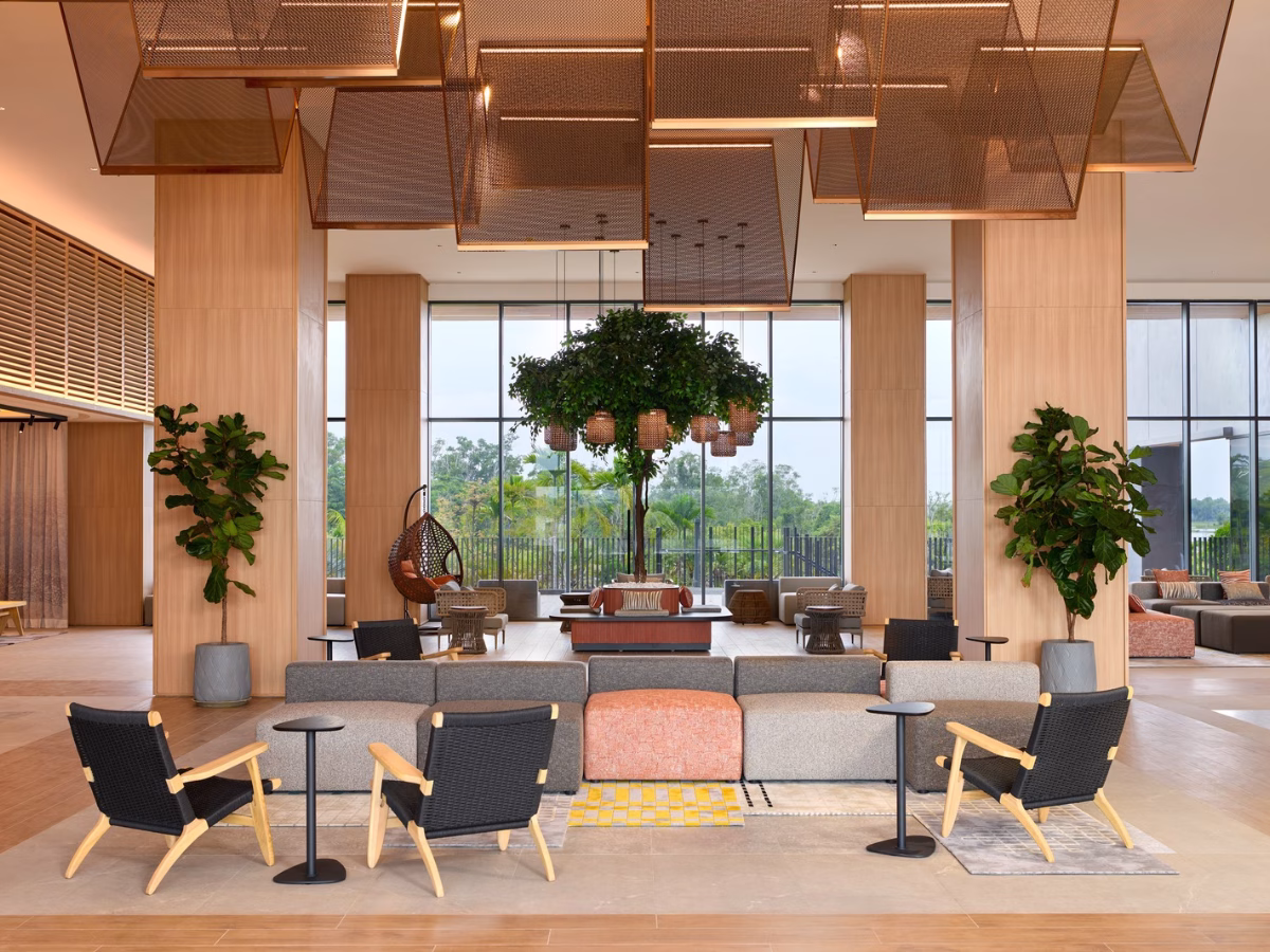 Lobby lounge at ASAI Gamuda Cove featuring contemporary sofas, rattan chairs, indoor greenery and floor-to-ceiling windows overlooking the landscape.