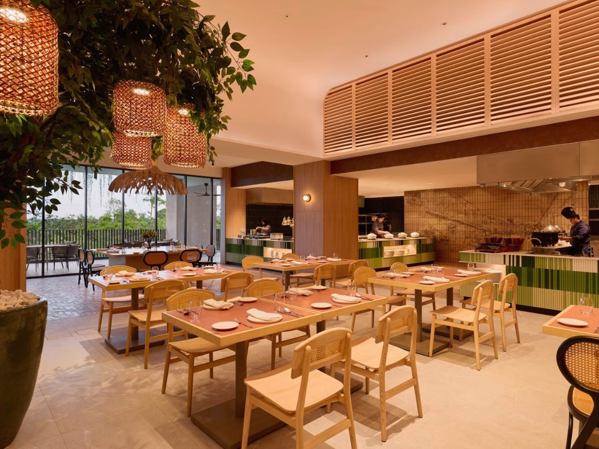 The interior of Nasi & Khao restaurant at ASAI Gamuda Cove, featuring wooden dining tables, rattan chairs, warm lighting and an open buffet counter.