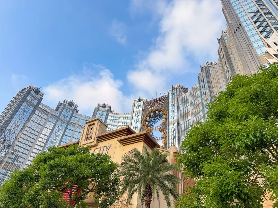 Studio City Macau resort towers and iconic Golden Reel Ferris wheel against a blue sky.